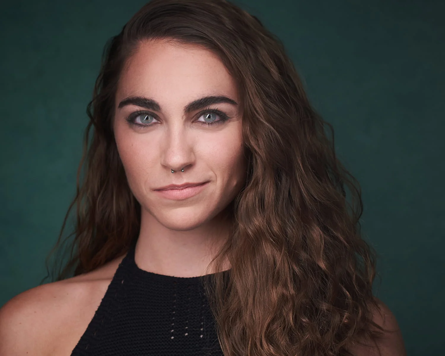 Female actor with subtle smile and thoughtful expression in black sleeveless top against teal background — commercial headshots