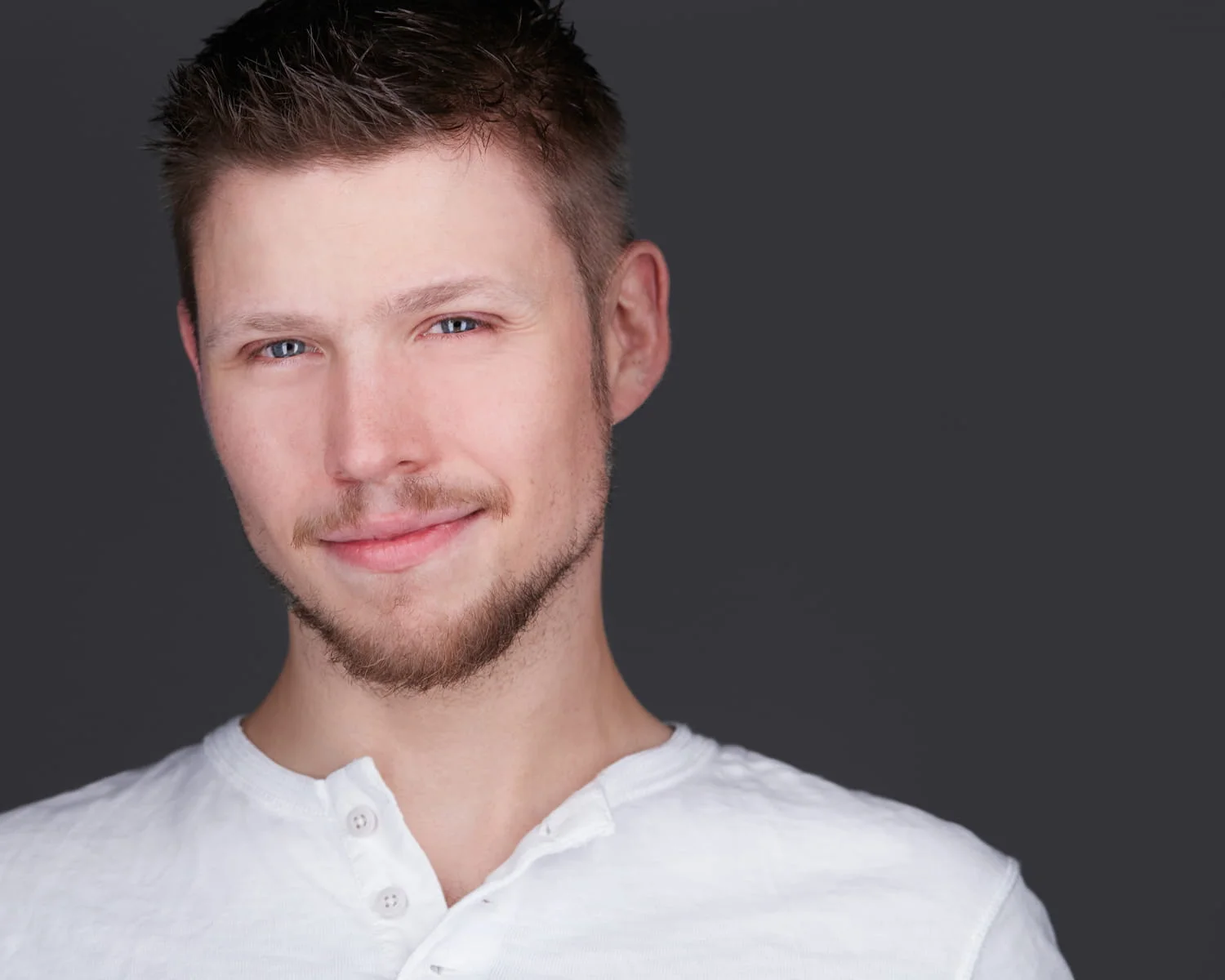 Male actor with friendly smile in white henley against dark gray studio background — Philadelphia actors headshot photographer