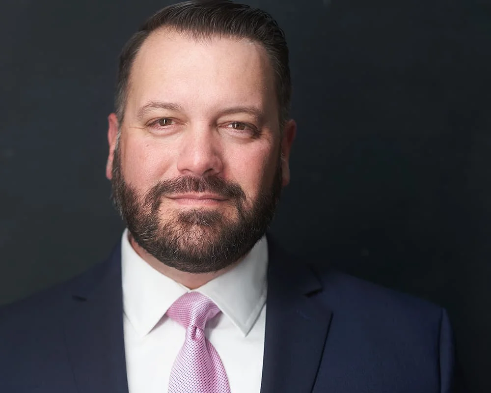 Bearded male executive in navy blazer, white shirt, and pink tie