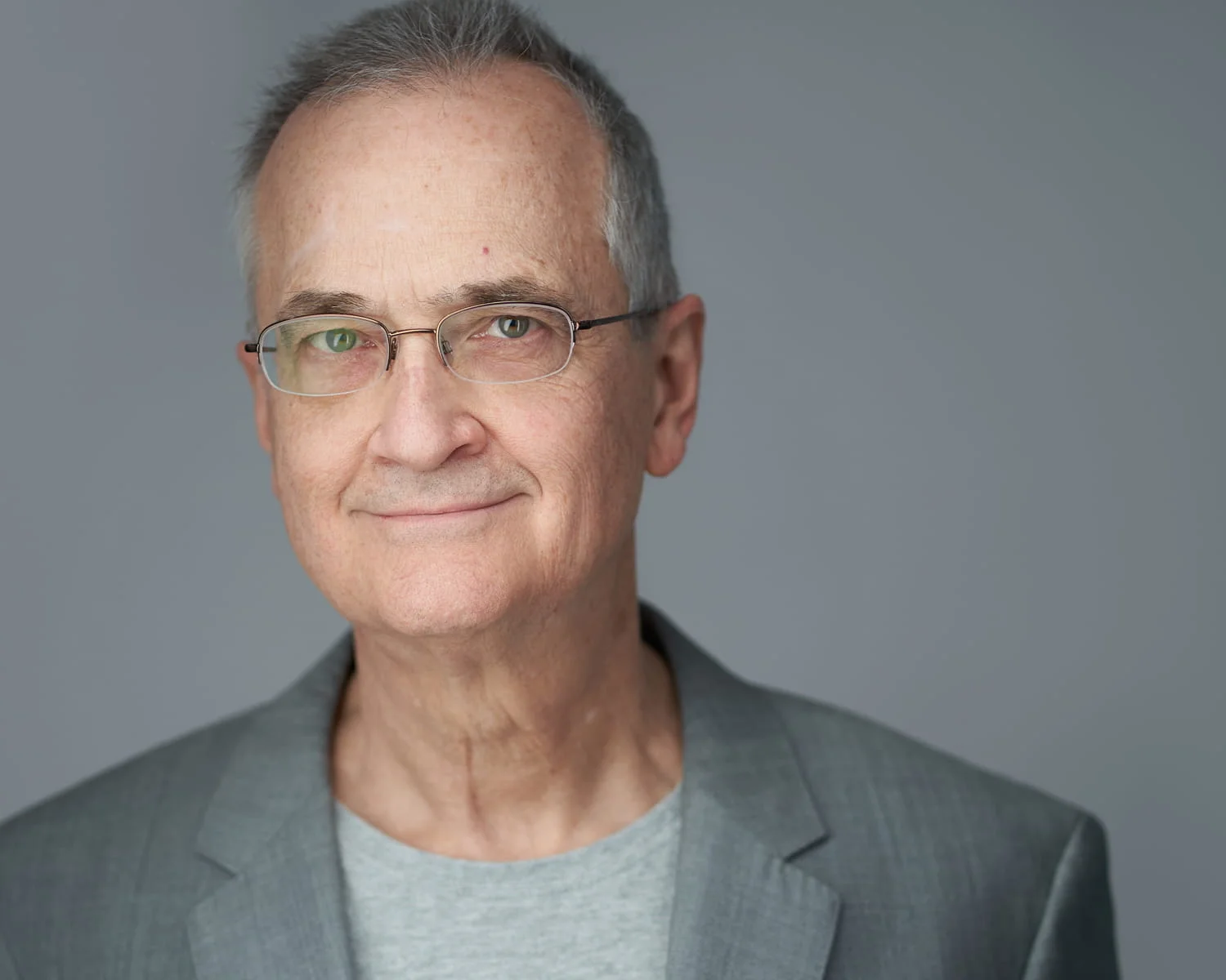 Professional male in gray blazer and gray t-shirt with warm expression against neutral studio background — personal branding portrait